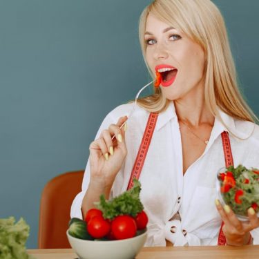 Woman enjoying a fresh salad with tomatoes and greens, promoting healthy eating.
