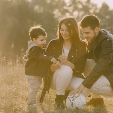 A cheerful family bonding outdoors with a soccer ball, enjoying a sunny day in the grass.